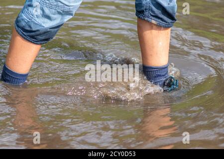 Ragazzo giovane che guidi attraverso l'alta marea con gumboot blu dopo un'alluvione ha rotto la diga di protezione e traboccante il paesi bassi o costa dell'oceano Foto Stock