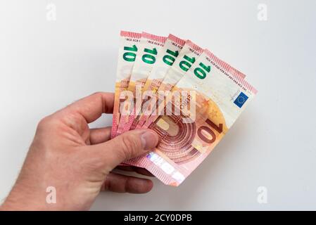 Mano di un uomo che detiene un mazzo di banconote da 10 euro come ricompensa, credito o reddito di lavoro secondario con un fondo bianco offuscato che mostra in somma 50 euro Foto Stock