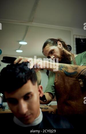 Un barbiere che si concentra sul taglio dei capelli di un cliente. barber concetto Foto Stock