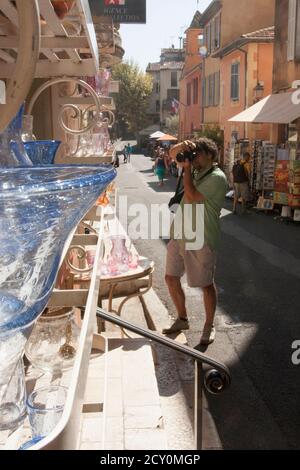 Sotto i negozi della strada del centro, i pezzi artistici sono realizzati in laboratori di soffiatura del vetro e collocati su scaffali e vetrine. Fotografo uomo dai capelli ricci Foto Stock