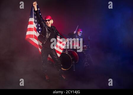 Foto di due pensionato gruppo di leggenda rock uomo donna energico fotografando hold america national flag play batteria strumenti indossare trendy pelle basculante Foto Stock