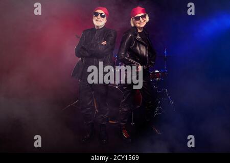 Foto di due pensionato gruppo di leggenda rock uomo donna energico concerto di tutta la vita sul palco che fotografa strumenti a tamburo dietro l'usura pelle basculante alla moda Foto Stock