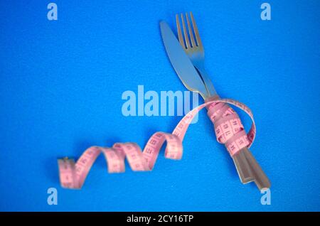 La forcella e il coltello sono avvolti in un nastro di misurazione rosa su sfondo blu Foto Stock