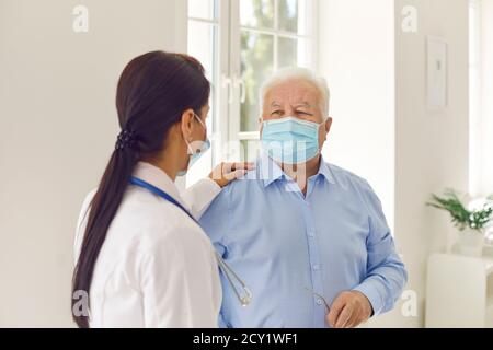Paziente anziano e giovane dottoressa, indossando maschere mediche per il viso, comunicando in ospedale Foto Stock