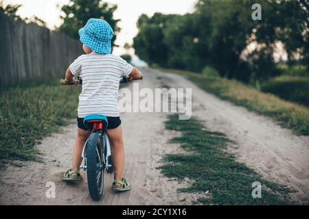 Indietro foto di un ragazzo caucasico in bicicletta indossare un cappello e camminare su una strada di campagna Foto Stock