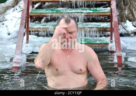 Uomo adulto che si batte prima di tuffarsi in acqua ghiacciata durante la festa Epifania sul fiume Dnipro. 19 gennaio 2017. Kiev, Ucraina Foto Stock