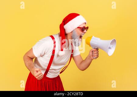 Profilo ritratto eccitato grigio nervoso uomo bearded in babbo natale cappello urlando tenendo altoparlante megafono, divertendosi a celebrare le vacanze invernali. Foto Stock