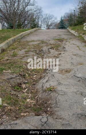 Cattiva strada asfaltata nel parco in una giornata invernale. Attraverso l'asfalto rotto l'erba cresce Foto Stock