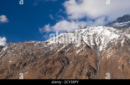 Paesaggio della montagna del Caucaso. Le cime rocciose ricoperte di neve sono sotto il cielo blu durante il giorno di sole. Comune di Kazbegi, Georgia Foto Stock