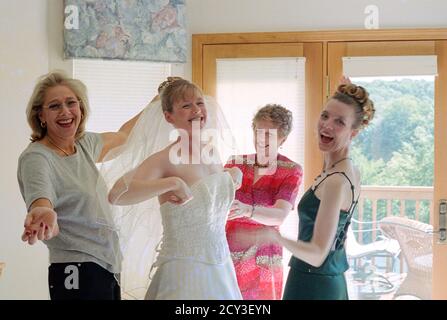 La madre e gli assistenti nuziali assistono la giovane sposa con il suo abito da sposa prima della cerimonia, USA 2001 Foto Stock