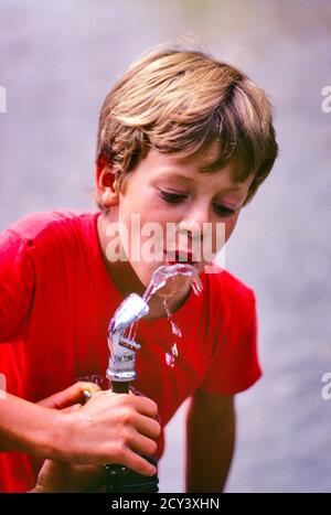 ANNI '70 TREDICI BIONDO PRESTEEN RAGAZZO CON T-SHIRT ROSSA REIDRATANTE BERE ACQUA FRESCA E PULITA E RINFRESCANTE DA FONTANA ALL'APERTO - CJ00884 CAM001 HARS BIONDA SICUREZZA COOL SICUREZZA GIOIA VITA SANA COPIA SPAZIO MEZZA LUNGHEZZA MASCHI RISCHIO ESPRESSIONI FELICITÀ BENESSERE PROTEZIONE ALLEGRA ESTERNO RICREAZIONE CAM001 PRESEPIO SORRISI CONCETTUALI IDRATAZIONE GIOIOSO T-SHIRT GIOVANI PRE-TEEN RAGAZZO RINFRESCANTE RELAX TREDICI ETNIA CAUCASICA VECCHIO STILE Foto Stock