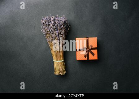 Bouquet di lavanda e confezione regalo con nastro su sfondo nero. Fiori secchi e una scatola a sorpresa. Vista dall'alto, layout piatto Foto Stock