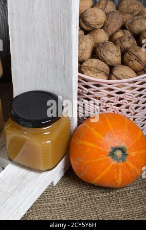 Marmellata di frutta in vasi. Si erge in una scatola di legno dipinta di bianco. Accanto si trova un cestino di noci e una zucca arancione. Foto Stock