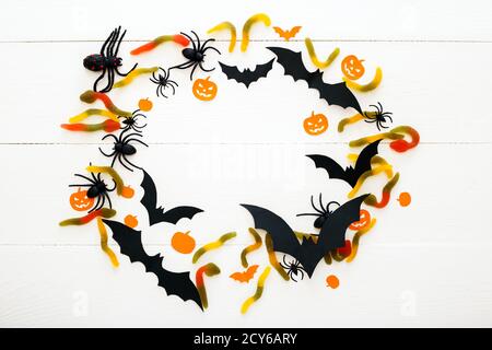 Sfondo di Halloween con caramelle dolci, vermi, pipistrelli di carta, ragni, zucche di papà su sfondo bianco di legno. Decorazioni per le vacanze di Halloween. Disposizione piatta Foto Stock