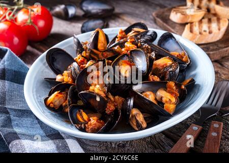 Deliziose cozze in stile cajun jambalaya con salsiccia, sedano, cipolla, pepe e pomodoro su un tavolo rustico. Foto Stock