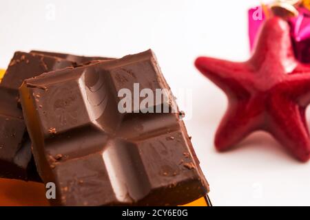 Primo piano di pezzi di barrette di cioccolato a sinistra dell'immagine e una stella rossa in una sfocatura sullo sfondo a destra Foto Stock