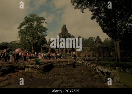 Turisti in fila in gruppi, entrando Prasat Bayon complesso tempio al centro di Angkor Tom antica città in Siem Reap provincia della Cambogia. Foto Stock