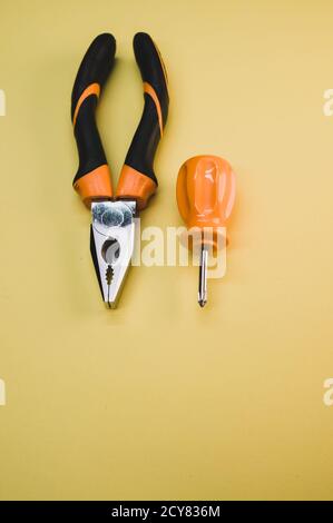 Vista dall'alto di un cacciavite piccolo con pinze isolate uno sfondo giallo Foto Stock