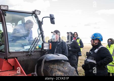 Aylesbury vale, Regno Unito. 1 ottobre 2020. Un agricoltore in un movimentatore di teleobiettivo chiede ai Bailiffs del National Eviction Team che lavorano per conto di HS2 Ltd per chiarimenti sul motivo per cui stanno costruendo una recinzione attraverso il suo campo durante lo sfratto di attivisti anti-HS2 da un campo di protezione della fauna selvatica in un antico bosco a JonesÕ Hill Wood. Circa 40 attivisti ambientali e residenti locali, alcuni dei quali vivono in case di alberi di fortuna a circa 60 metri sopra il suolo, erano presenti durante gli sfratti a JonesÕ Hill Wood che aveva servito come uno dei numerosi campi di protesta allestiti lungo il percorso del £106bn HS2 high-sp Foto Stock