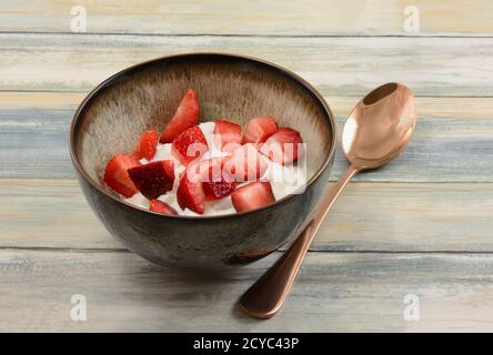 Fragole fresche tagliate e yogurt greco puro in recipiente con cucchiaio di rame Foto Stock