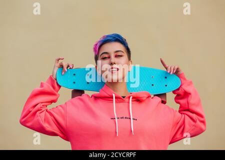 Giovane donna elegante che tiene lo skateboard sulle spalle. Concetto di gioventù. Foto Stock