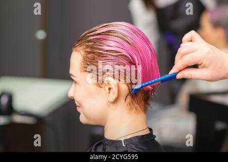 Giovane donna che riceve trattamento dei capelli dopo colorazione rosa a mano di parrucchiere maschile in parrucchiere Foto Stock