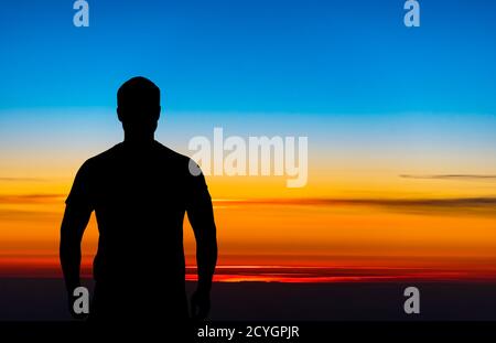 Silhouette di un uomo, lato posteriore, in piedi davanti al bel cielo durante il tramonto Foto Stock