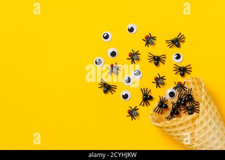 Ragni neri e mosche, gli occhi d'oca strisciano fuori del cono del gelato su sfondo giallo Top view Flat Lay Happy Halloween idea creativa Holiday card Foto Stock