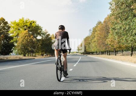 Uomo su una bici di ghiaia sulla strada, vista posteriore. Ciclista ben attrezzata che guida una bicicletta moderna all'aperto Foto Stock