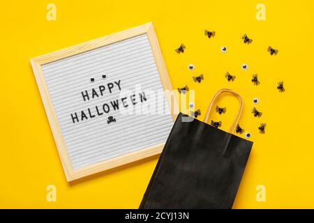 Felt board con testo e pacchetto nero, ragni striscianti su sfondo giallo Top view Flat Lay Happy idea creativa Halloween Holiday card Foto Stock