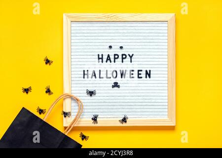 Felt board con testo e pacchetto nero, ragni striscianti su sfondo giallo Top view Flat Lay Happy idea creativa Halloween Holiday card Foto Stock