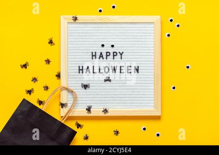 Felt board con testo e pacchetto nero, ragni striscianti su sfondo giallo Top view Flat Lay Happy idea creativa Halloween Holiday card Foto Stock