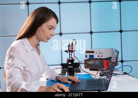 Donna studente con robot industriale braccio nel laboratorio di progettazione Foto Stock