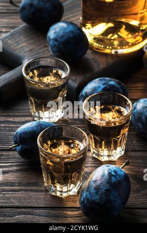 Slivovica - brandy di prugne o vodka di prugne, liquore duro, bevanda forte in bicchieri su vecchio tavolo di legno, prugne fresche, spazio di copia Foto Stock