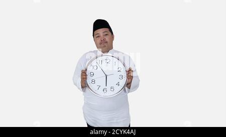 musulmano asiatico con sovrappeso in piedi e tenere grande orologio rotondo in attesa di pausa digiuno. islam ragazzo grasso non può aspettare per mussulmano pausa digiuno conc Foto Stock