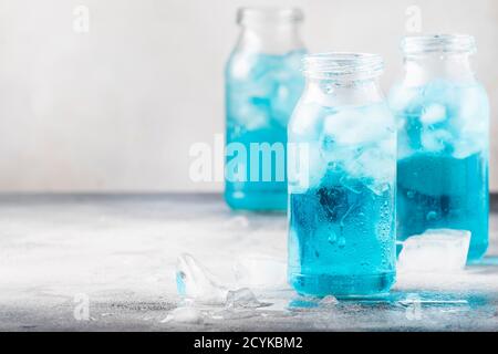 Concetto di bevanda sportiva e fitness, acqua blu isotonica fredda in bottiglie, sfondo grigio della tavola, fuoco selettivo Foto Stock