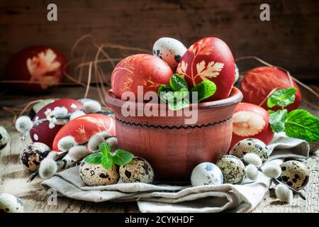 Marrone uovo di pasqua con un modello con piccole uova di quaglia speckled in una ciotola di argilla con foglie di menta e spriggs di salice soffice, ancora vita in un paese st Foto Stock