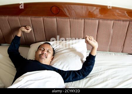 Uomo asiatico che si sveglia al mattino. Ragazzo asiatico stretching e sbadigliare a letto Foto Stock