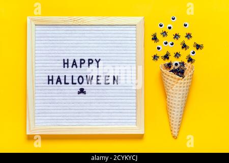 Felt board con testo, citazione, ragni neri e mosche, occhi d'oca strisciare fuori del cono gelato su sfondo giallo Top view Flat Lay Happy Halloween Foto Stock