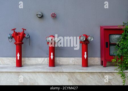 Set di diversi idranti antincendio rossi all'esterno sulla parete grigia. Angolo di sicurezza antincendio con l'attrezzatura estintore necessaria. Foto Stock