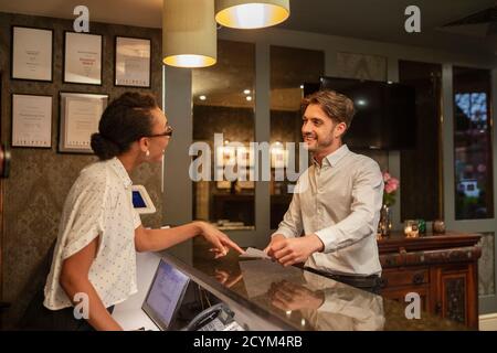 Un addetto alla reception dell'hotel che parla con un cliente che effettua il check-in in hotel. Foto Stock