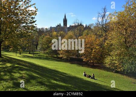 Tre studentesse che si rilassano al sole d'autunno nel Kelvingrove Park con l'edificio dell'Università di Glasgow, Scozia, Regno Unito Europa sullo sfondo Foto Stock