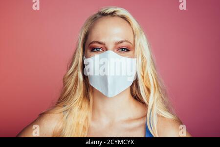 Primo piano di una donna con maschera protettiva su sfondo rosa. Bella donna indossare maschera protettiva. Foto Stock