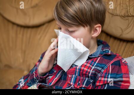 teenager che soffia il suo naso che cola in fazzoletto di carta del tessuto a casa. Naso che cola cronico nel bambino sintomo del virus respiratorio covid-19. Assistenza sanitaria, Foto Stock