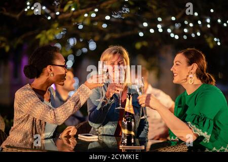 Gruppo di diverse amiche che bevono champagne all'aperto in un bar/ristorante, festeggiando e divertendosi insieme. Foto Stock