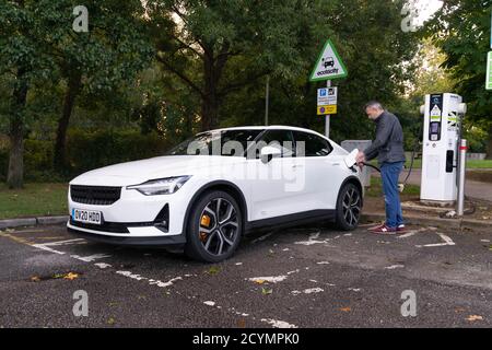 Uomo che carica un veicolo elettrico in un vano di ricarica per veicoli elettrici pubblico. Il veicolo è un Polestar 2 che presto prenderà il controllo della Model S di Tesla Foto Stock