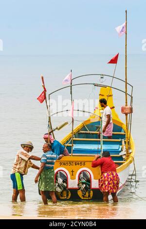 I pescatori che tirano la loro colorata barca da pesca a riva alla trafficata e popolare spiaggia di Marari; Mararikulam, Alappuzha (Alleppey), Kerala, India Foto Stock