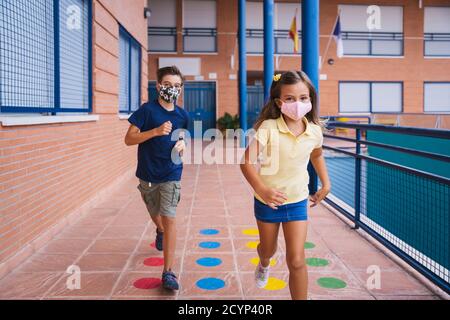 Ritorno a scuola. Bambini che corrono nel cortile con maschera facciale Foto Stock