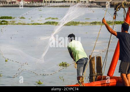 Fisherman casting circolare peso rete mano sul lungomare di Vypin Island di fronte Fort Cochin oltre; Fort Vypin, Kochi (Cochin), Kerala, India Foto Stock