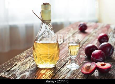 Brandy tradizionale balcanico di prugne - rakija o rakia slivovica in bottiglia, un wineglass con sljivovica e prugne fresche su sfondo ligneo in giorno Foto Stock